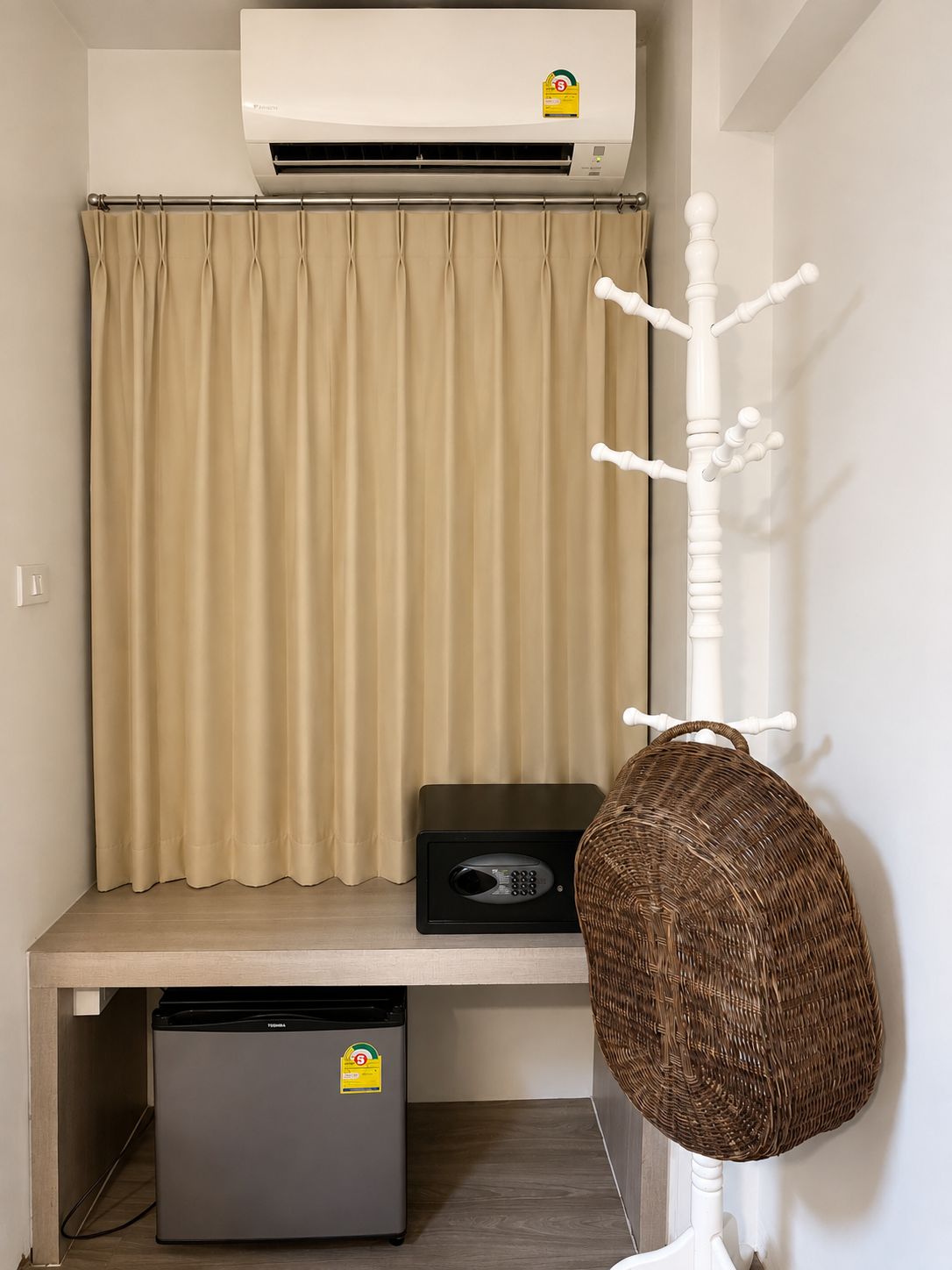 Une pièce avec un rideau beige, un porte-manteau blanc, un haut-parleur noir et un petit réfrigérateur.