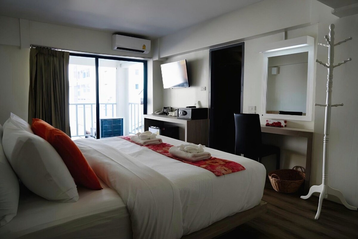 A hotel room with a bed, a desk, a TV, and a coat rack.