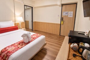 Ett hotellrum med en säng, ett skrivbord, en stol, en lampa, en garderob och en dörr.