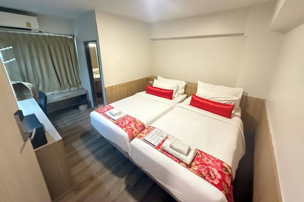 A hotel room with two beds, a desk, and a mirror.
