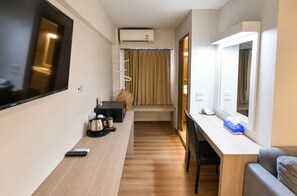 A compact hotel room with a flat-screen TV, a desk with a chair, a small kitchenette, and a seating area with a sofa.