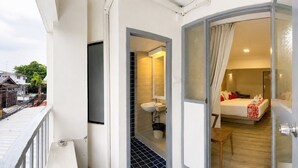 Ein Hotelzimmer mit Bett, Nachttisch, Stuhl, Badezimmer mit Waschbecken und Spiegel sowie ein Balkon mit Geländer.