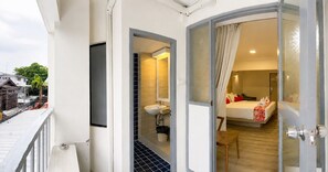 A hotel room with a bed, a bedside table, a chair, a bathroom with a sink and mirror, and a balcony with a railing. -  Wild Orchid Villa Bangkok (Bangkok)