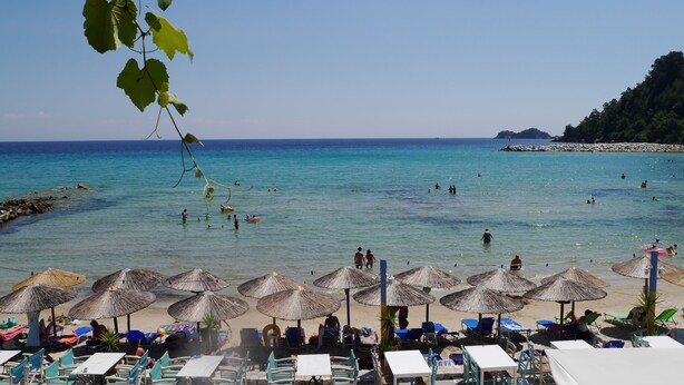 A beach with clear blue water, people swimming and sunbathing, and thatched umbrellas providing shade. - Blue Sea Beach Resort (Thasos)