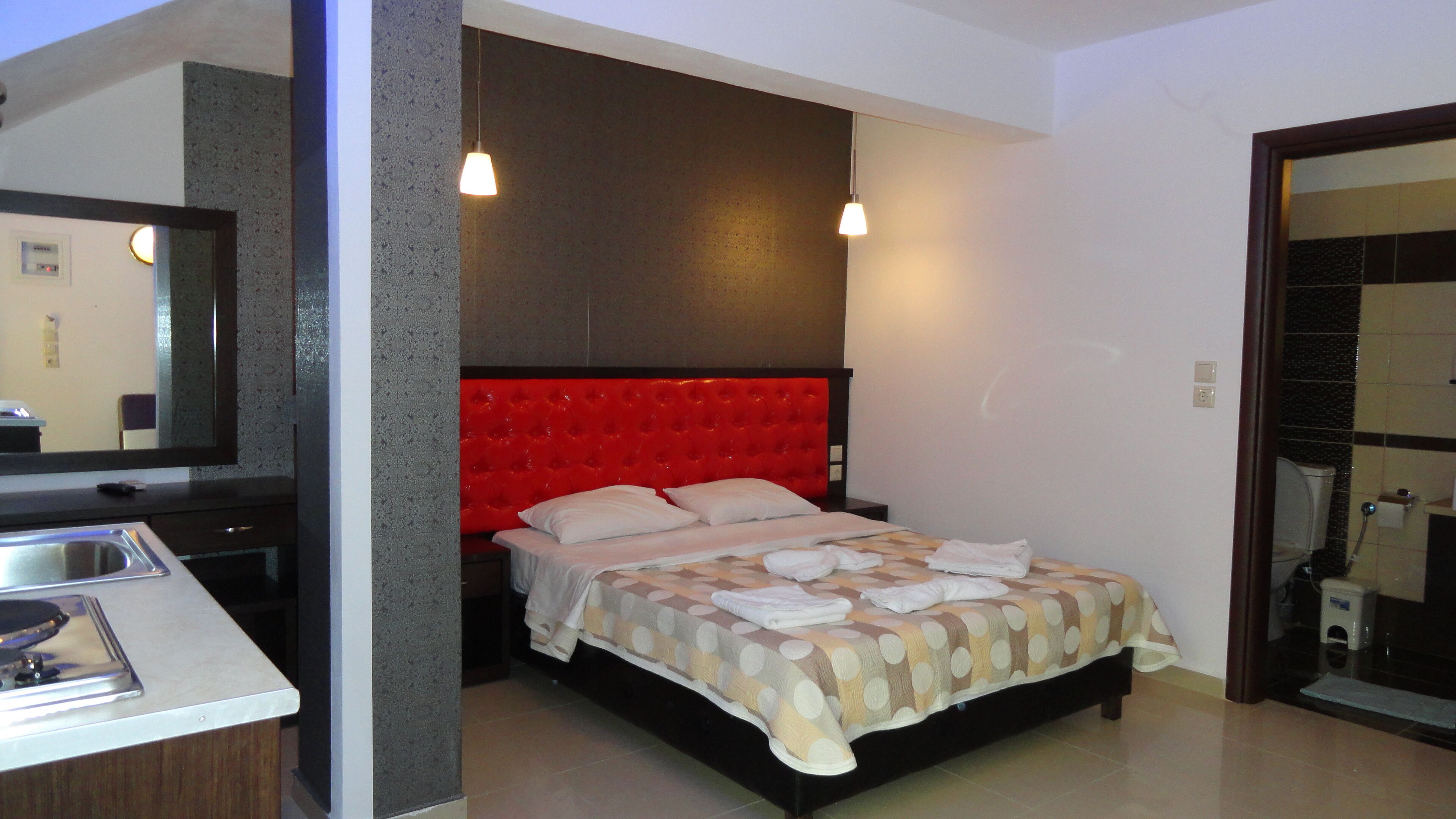 A modern bedroom with a red headboard, a bed with a polka dot bedspread, a bedside table, and a mirror.