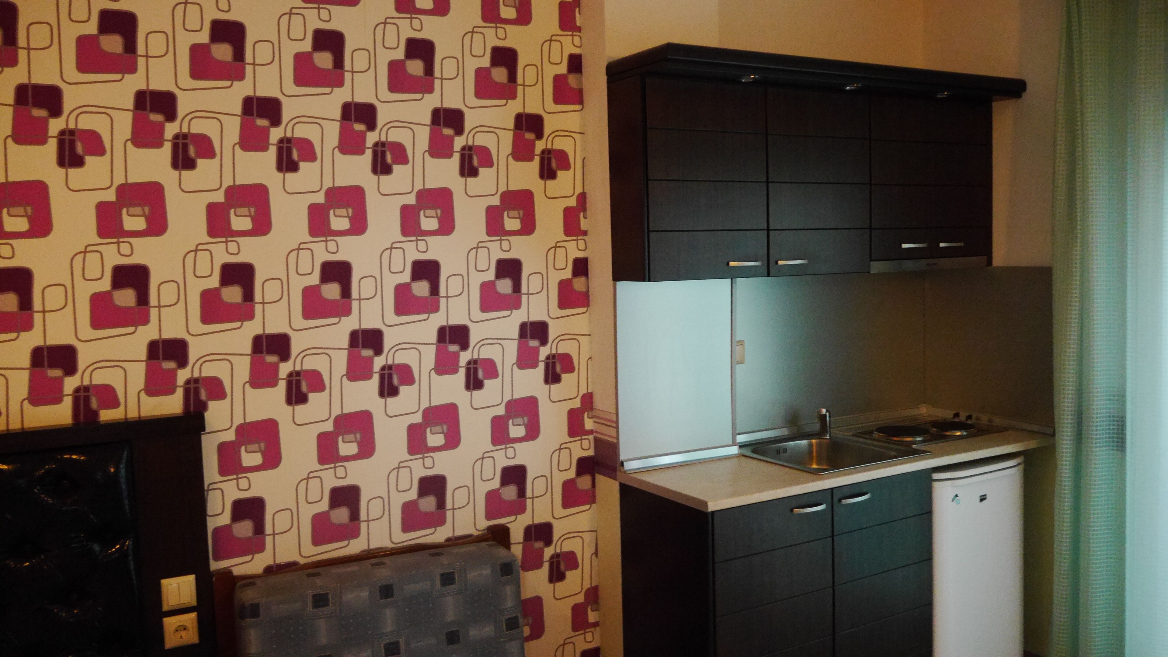 A kitchen with a patterned wallpaper, dark cabinets, a stainless steel sink, and a white dishwasher.