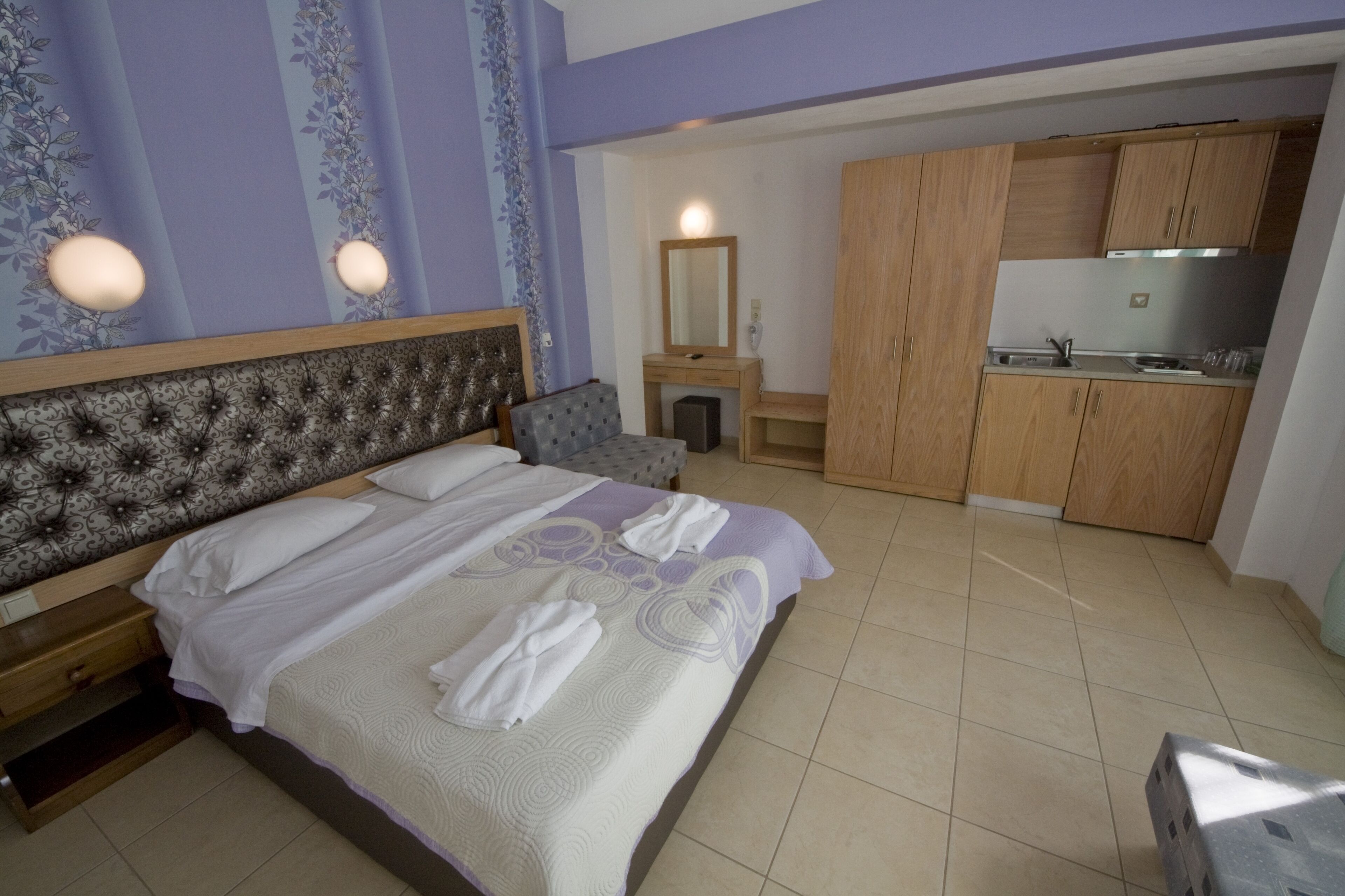 Ein Hotelzimmer mit Bett, Nachttisch, Sessel, Kommode und einer Küchenzeile.
