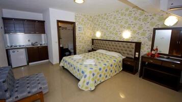 Un dormitorio con cama, mesita de noche y un pequeño escritorio con espejo. Hay una kitchenette con estufa y pileta.