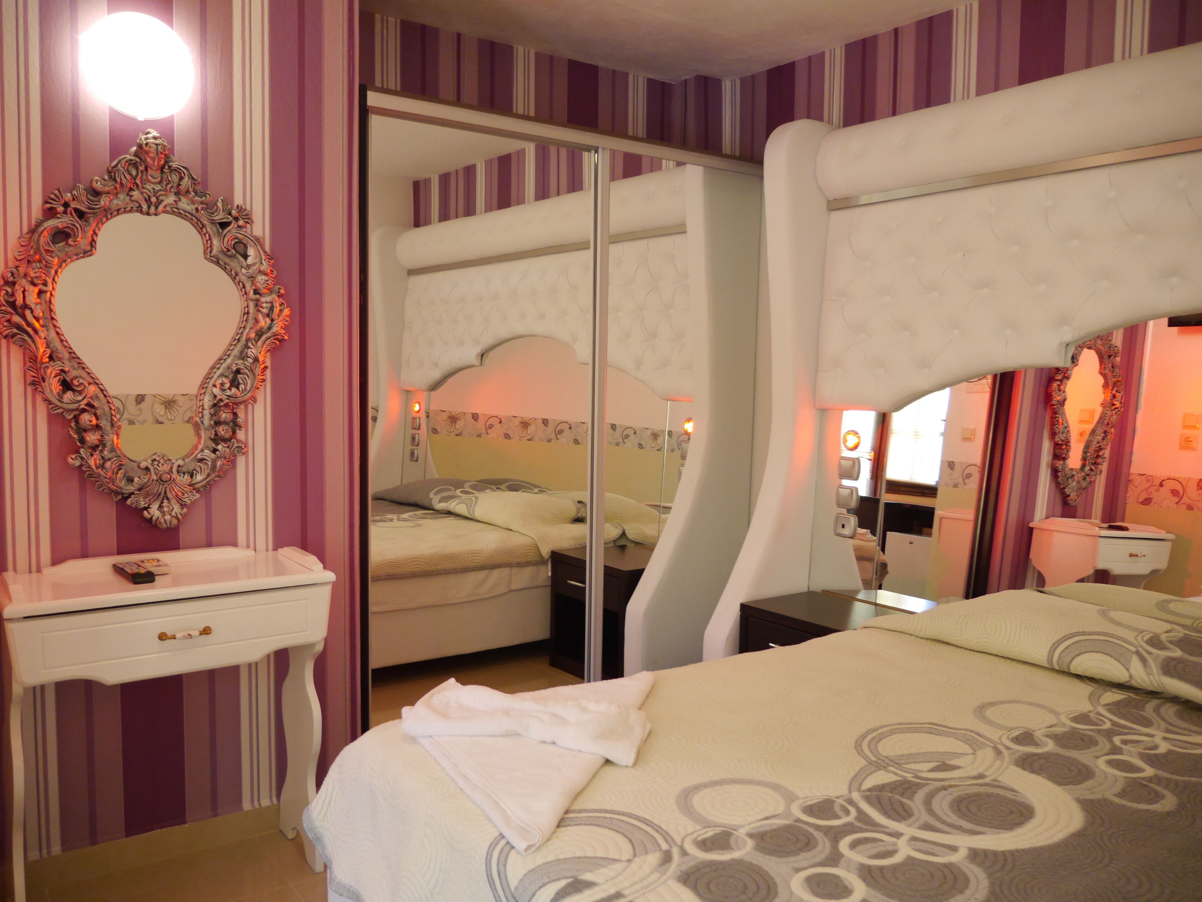 A bedroom with a large bed, a vanity with a mirror, and a small table.