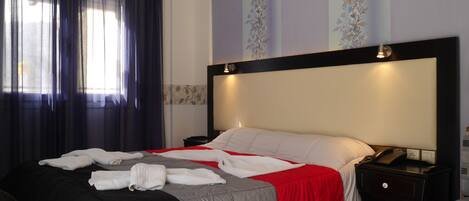 Una habitación de hotel con cama, mesita de noche, escritorio y ventana con cortinas.