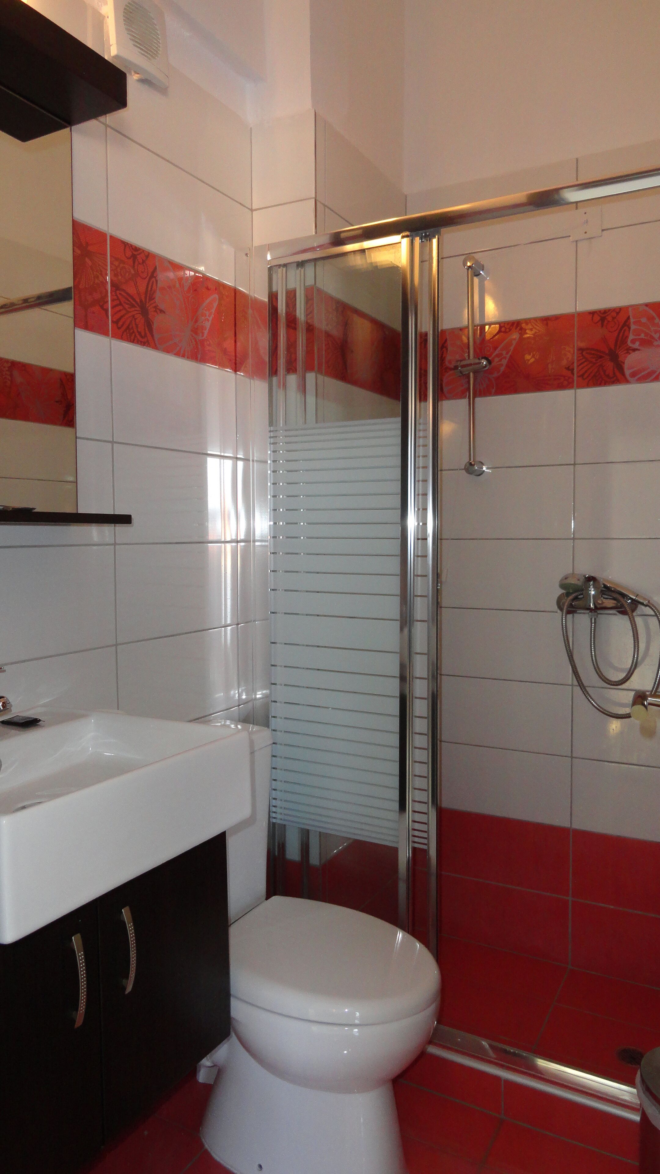 A bathroom with a white toilet, a glass-enclosed shower, and red-tiled walls.