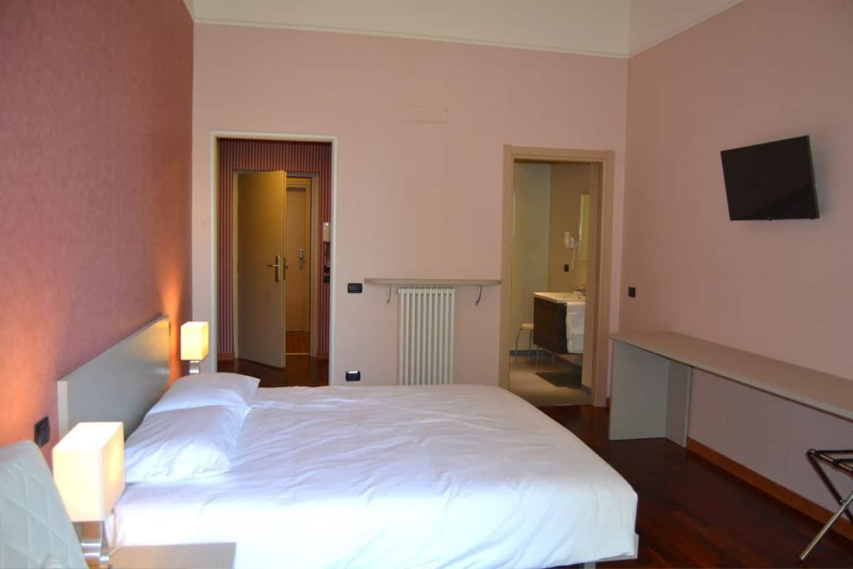 A hotel room with a bed, a desk, a chair, a TV, and a bathroom visible through an open door.