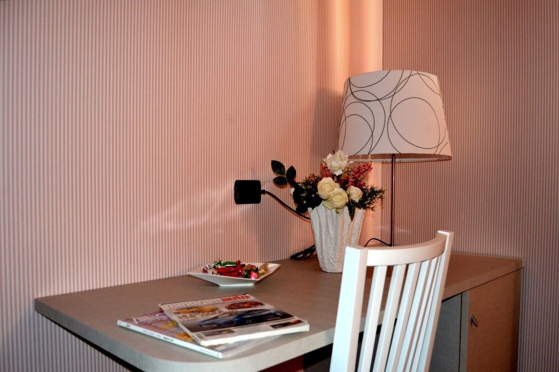 A room with a table, a chair, a lamp, a vase with flowers, and a magazine.