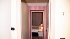 A narrow hallway leading to a bedroom with a bed, a nightstand, and a lamp. - Hotel Italia 30 (Gorgonzola)