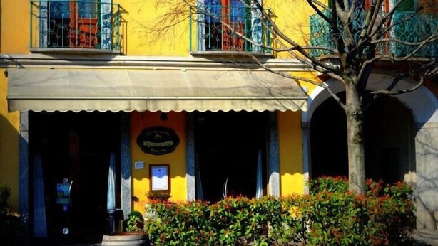 A yellow building with a balcony, a wooden barrel, and a stone planter. - Hotel Italia 30 (Gorgonzola)