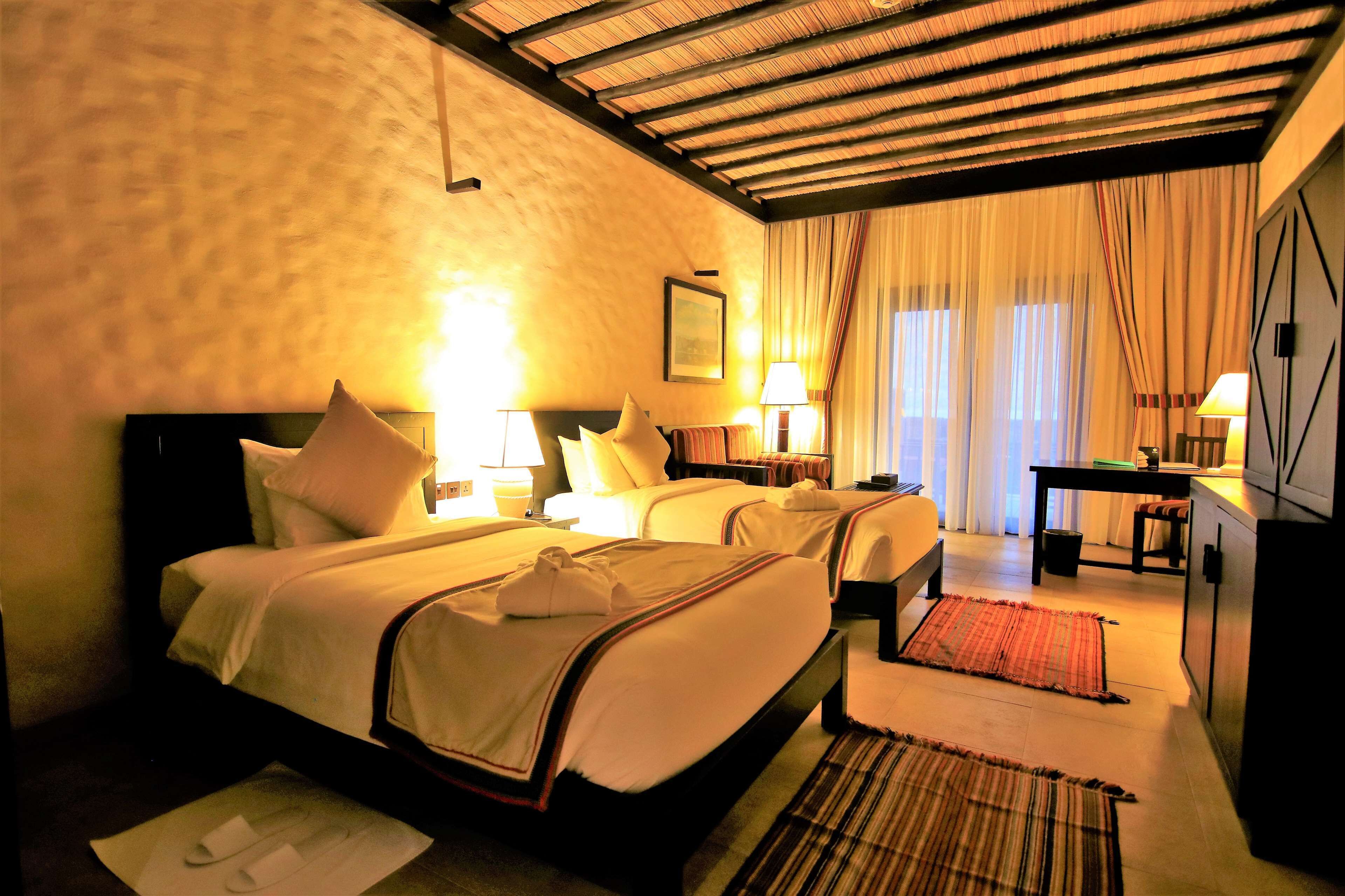 Habitación de hotel con dos camas, un escritorio, un televisor y una ventana con cortinas.
