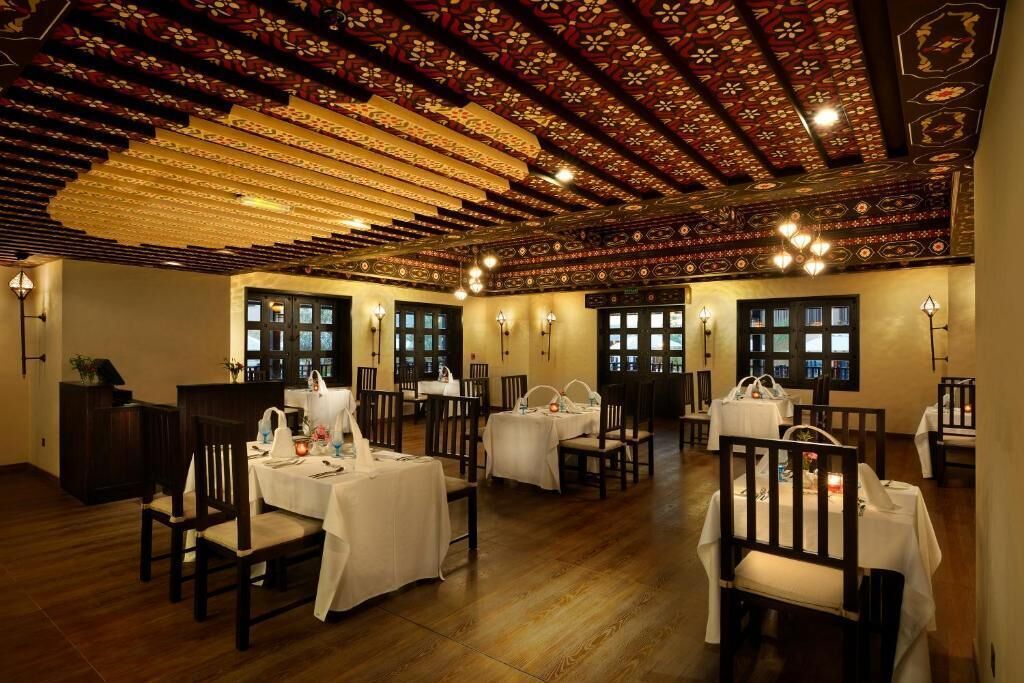 Un espace repas avec des tables dressées, des chaises en bois et un plafond orné de motifs.