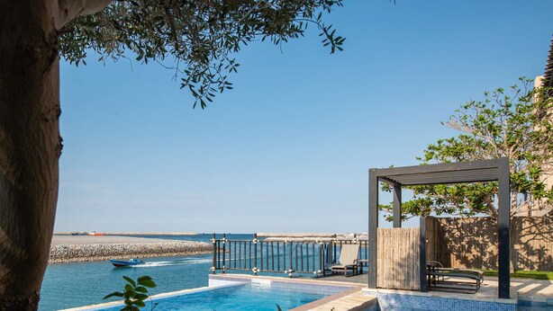 Una piscina con vistas al mar, una pérgola de madera y un área de descanso.