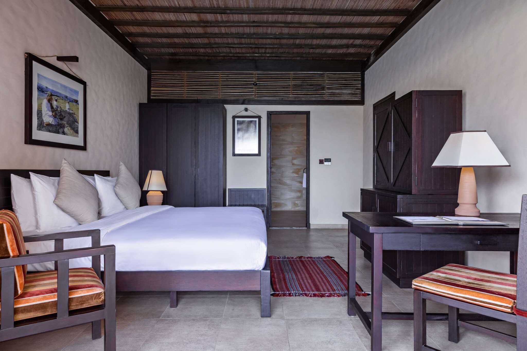 A hotel room with a bed, a desk, a chair, a TV, and a painting on the wall.