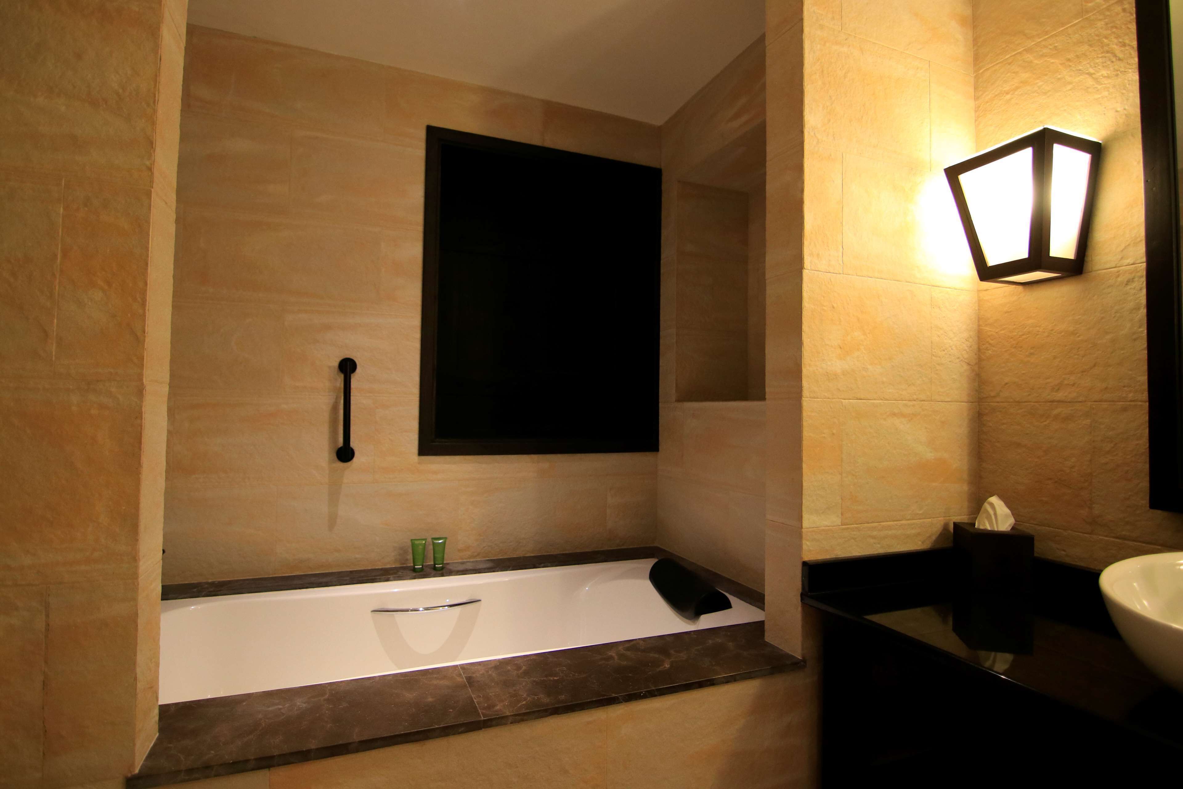 A modern bathroom with a bathtub, a wall-mounted light fixture, and a large mirror.