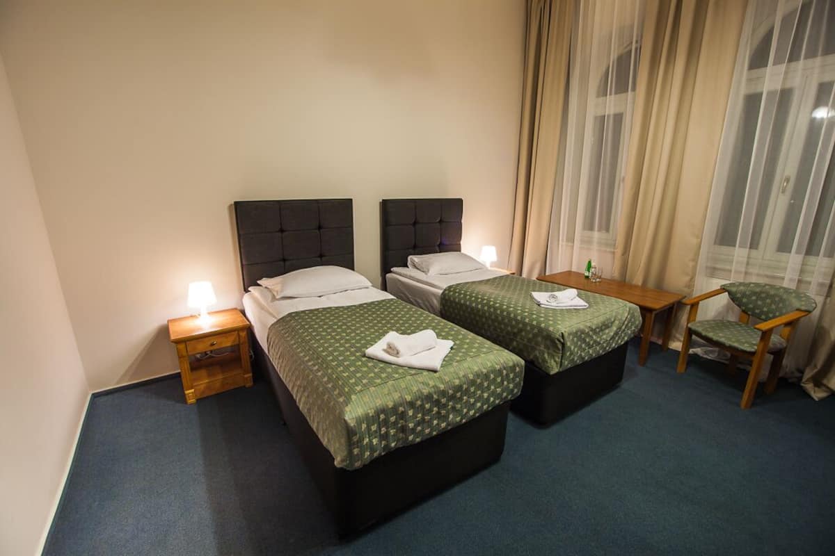 Ein Hotelzimmer mit zwei Betten, einem Holfnachtkästchen, einem kleinen Tisch und einem Sessel.