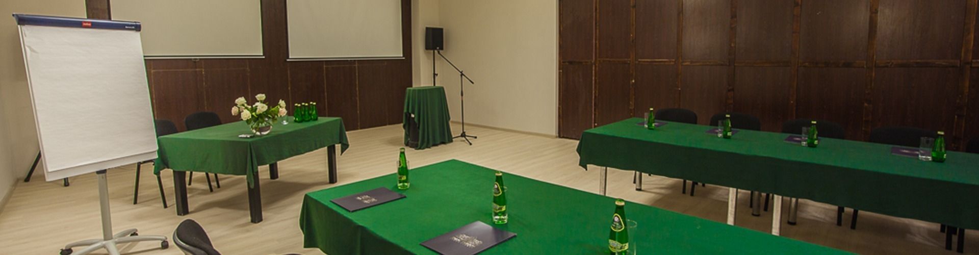 Une salle de conférence avec des tables vertes, des tableaux blancs et des arrangements floraux en guise de décoration.