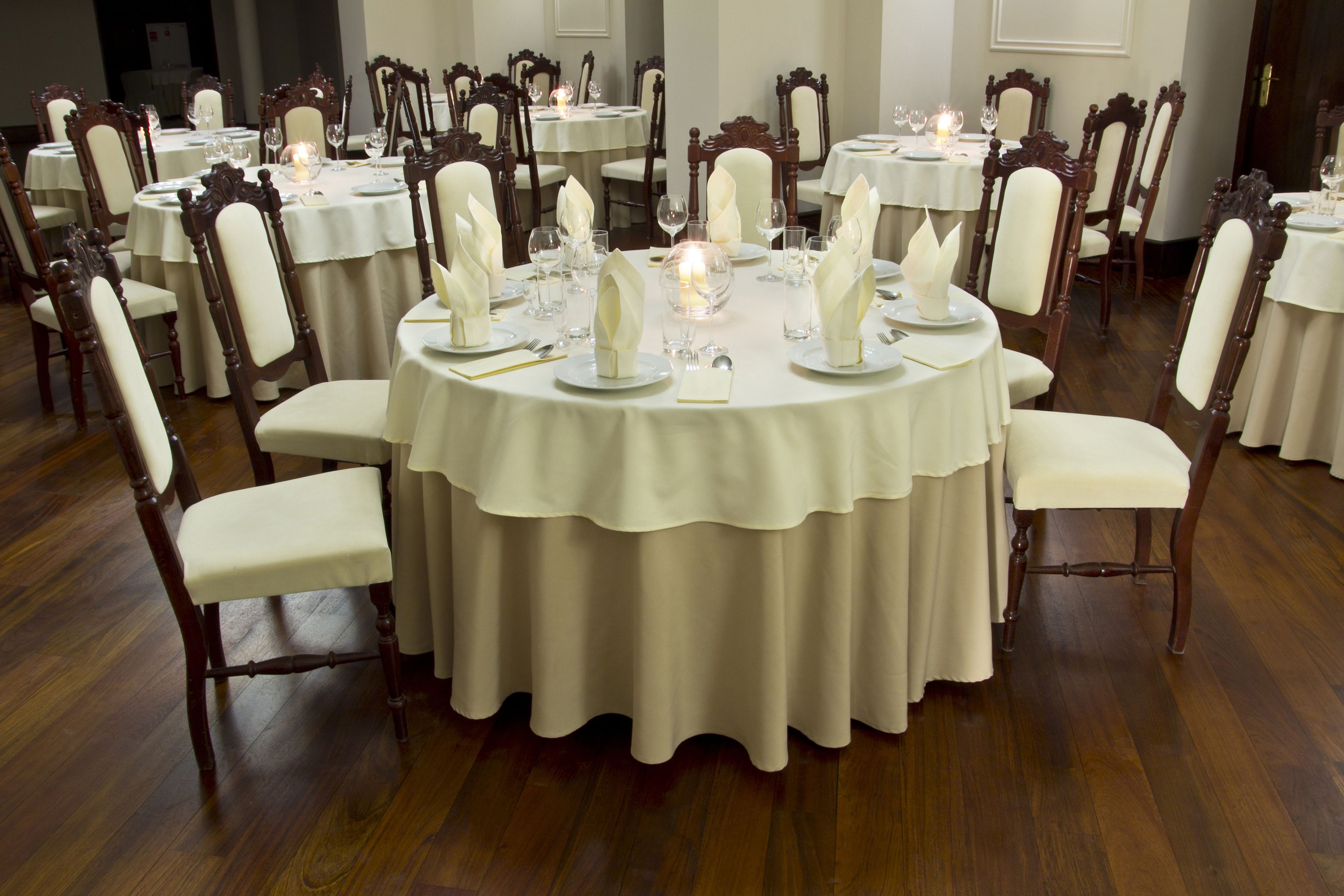 A formal dining room with round tables, white tablecloths, and wooden chairs.
