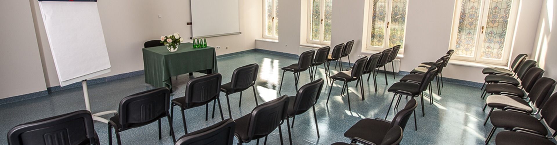 A conference room with rows of chairs, a table with a green tablecloth, and a whiteboard.