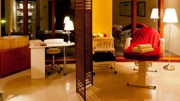 Comfortable seating area with a chair and a blanket, a bathroom with sink and mirror, and a large mirror reflecting the room's interior.
