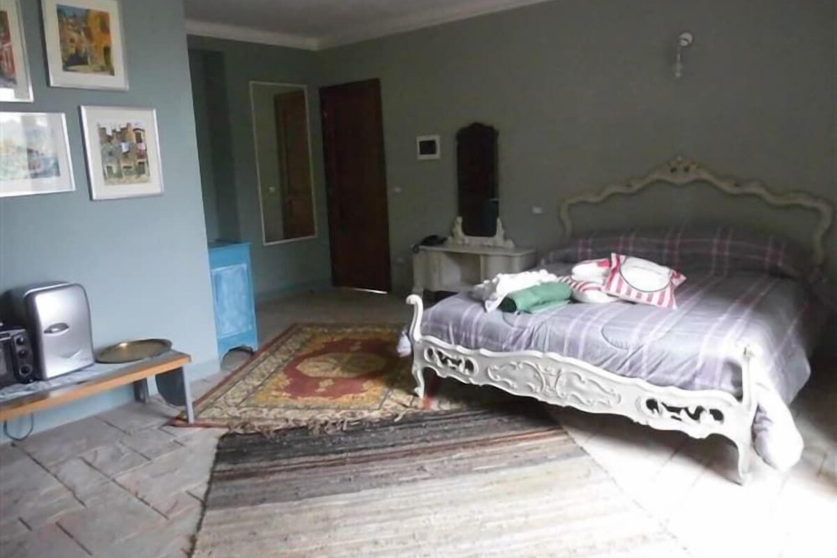 A bedroom with a bed, a bedside table, a mirror, and a wall with framed pictures.