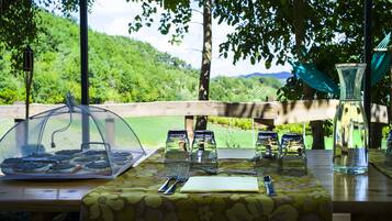 A table set outdoors with a view of a green landscape, a wooden fence, and a hammock.