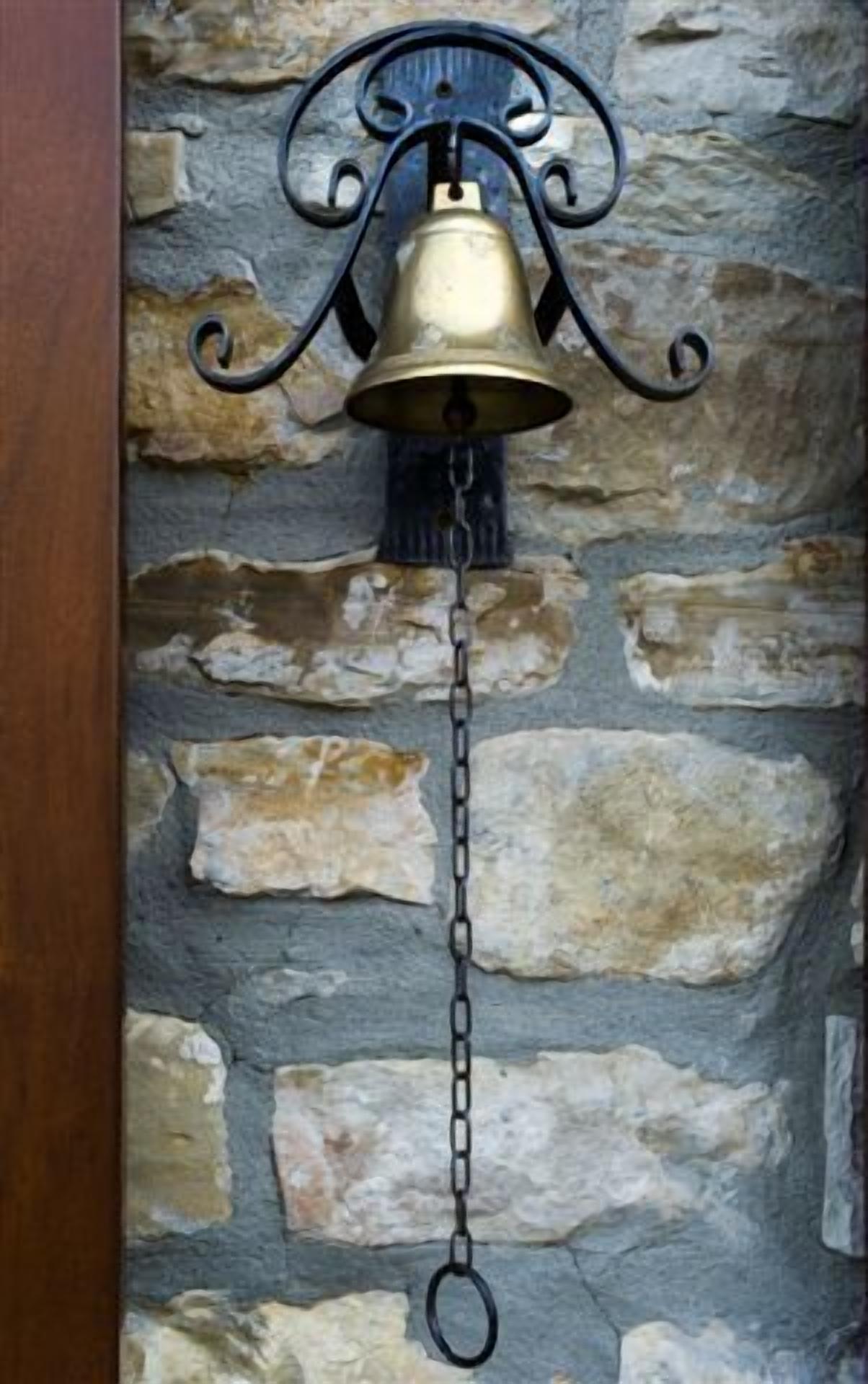 A wall-mounted bell with a chain, attached to a stone wall.