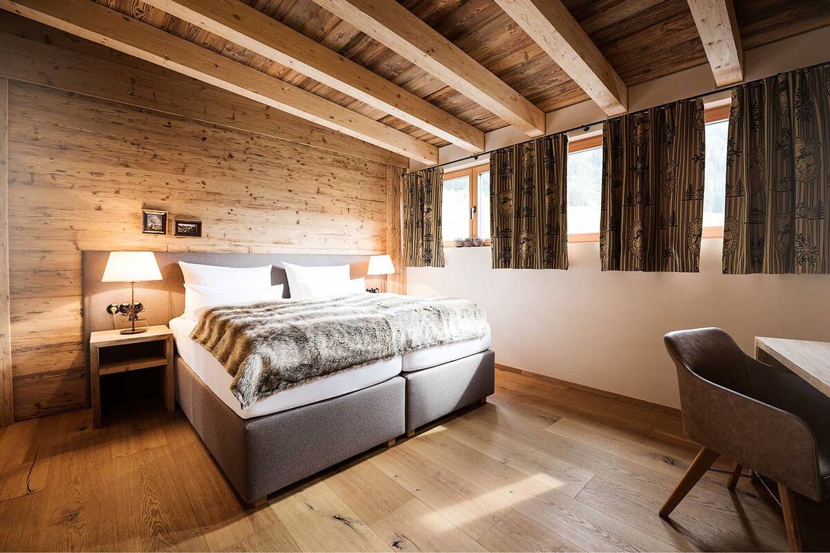 A bedroom with a wooden ceiling, a bed with a fur throw, two bedside lamps, and a chair.