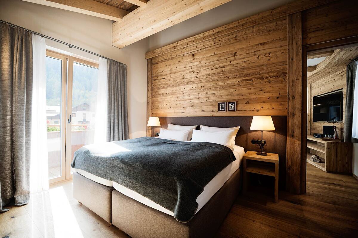 A bedroom with a wooden headboard, a bed with white linens, two bedside lamps, and a TV on a wooden stand.