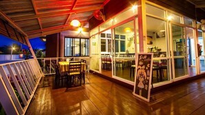 Un área de comedor al aire libre con mesas y sillas, una terraza de madera y un cerramiento de vidrio con un letrero que dice "S&M coffee".