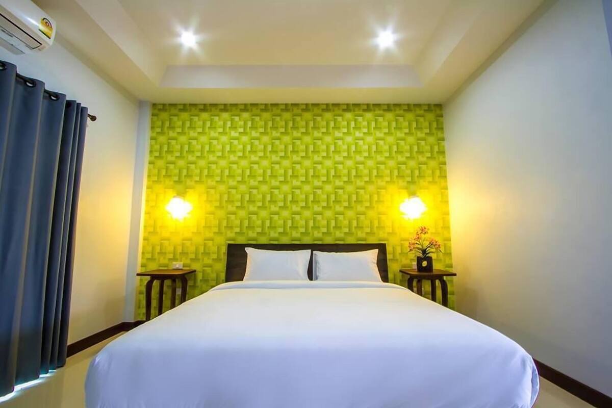 Ein Hotelzimmer mit einem großen Bett, zwei Nachttischen, einer Wand-Klimaanlage und einer Wand mit grünem Muster.