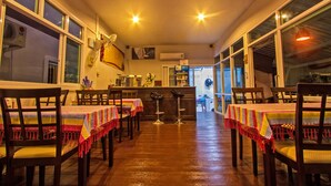 Un restaurante con mesas y sillas de madera, una zona de bar y grandes ventanales.