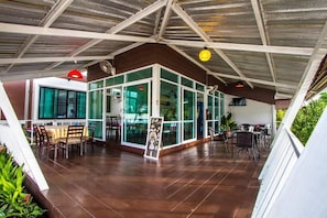 Un vaste espace intérieur doté d’un haut plafond et de murs en verre, aménagé avec des tables et des chaises disposées pour les repas ou les moments de convivialité.