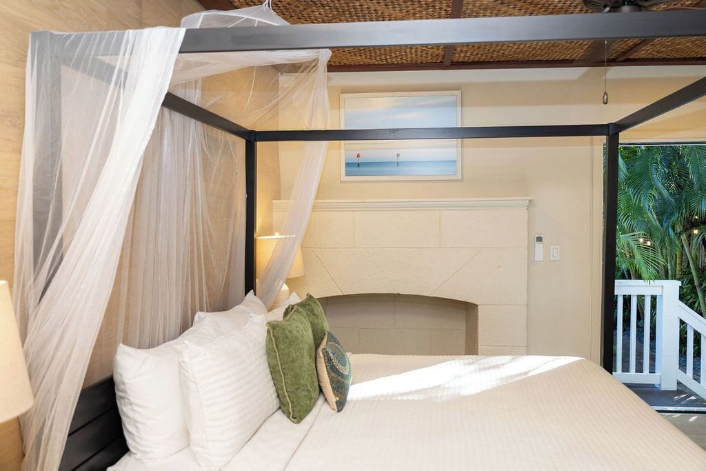A bedroom with a canopy bed, a view of the sea through a window, and a balcony with a railing.