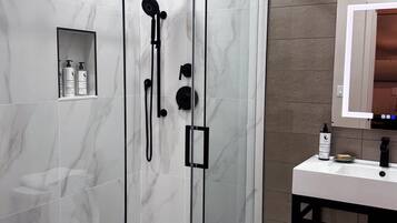 A modern bathroom with a glass-enclosed shower, a white sink, and a mirror above it.