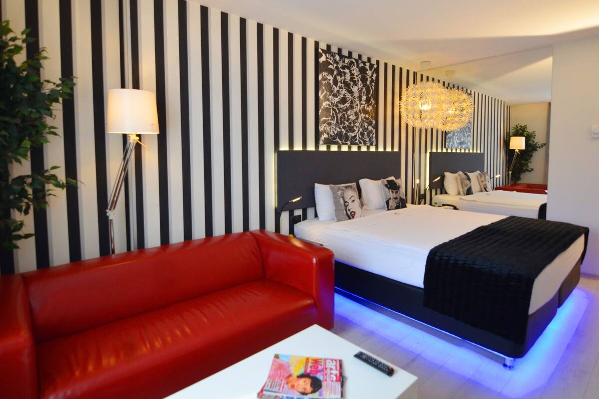 A hotel room with a red sofa, two beds, a large mirror, and a decorative wall panel.