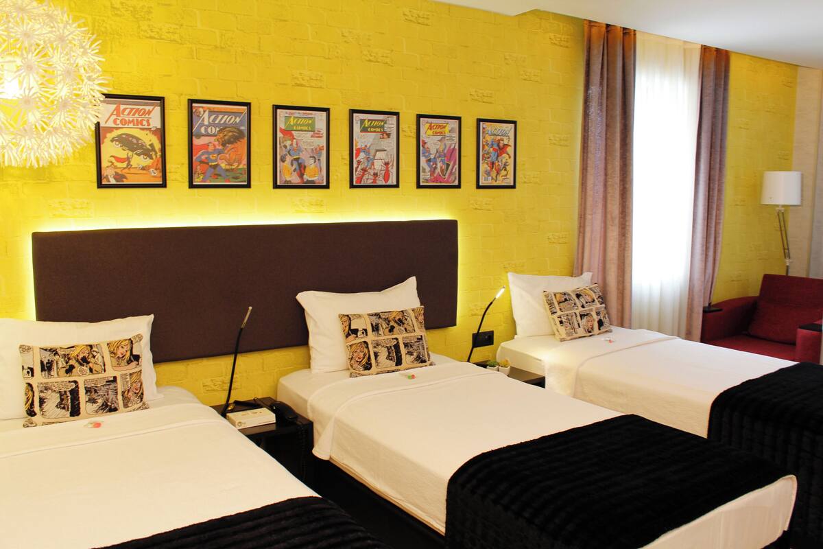 A hotel room with two beds, a large headboard, and a wall decorated with comic book posters.