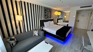 A hotel room with a striped wall, a sofa, a bed with a black headboard, a desk, and a chair. - Tempo Fair Suites (Istanbul)