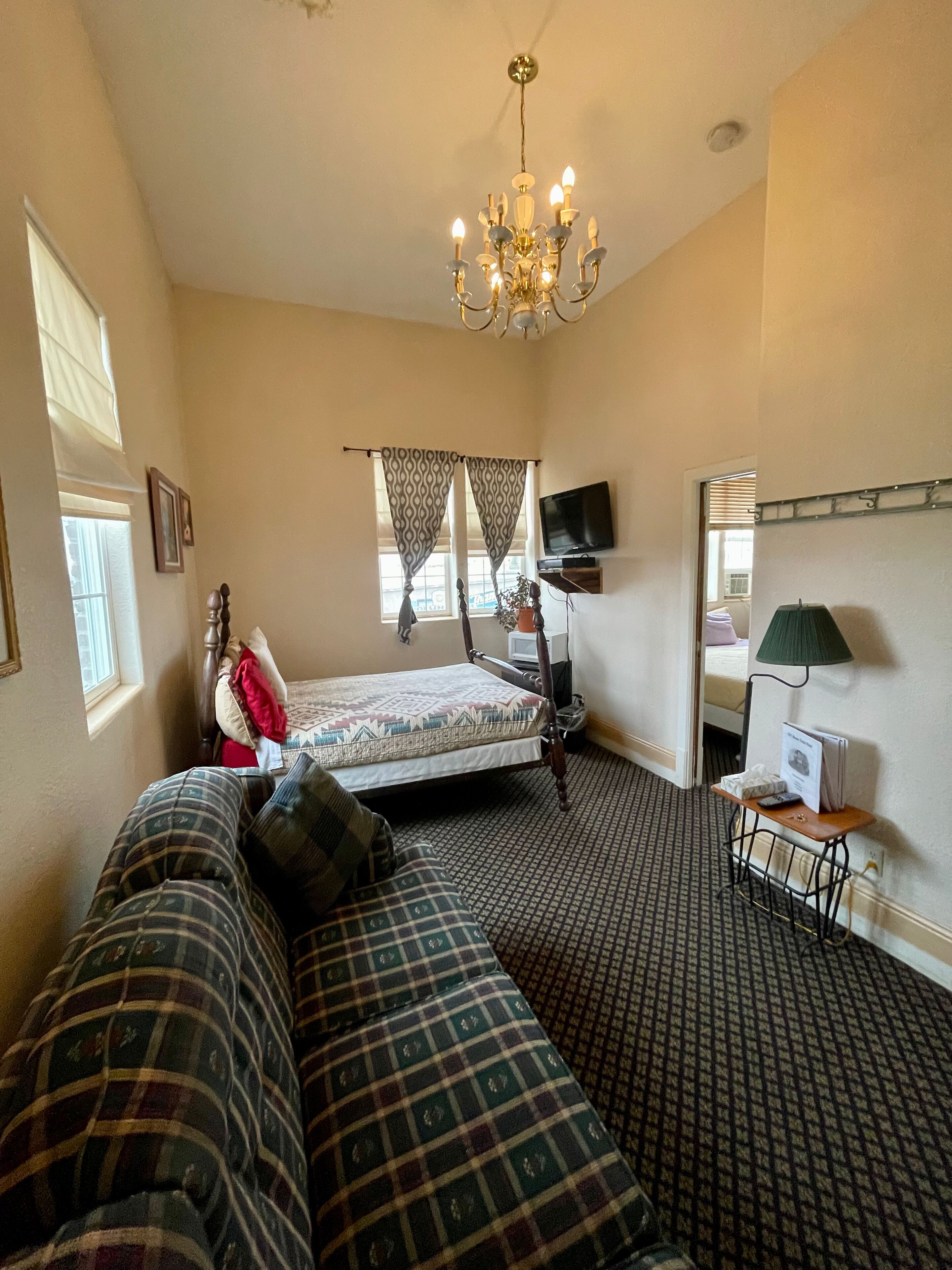 A hotel room with a bed, a sofa, a television, and a chandelier.