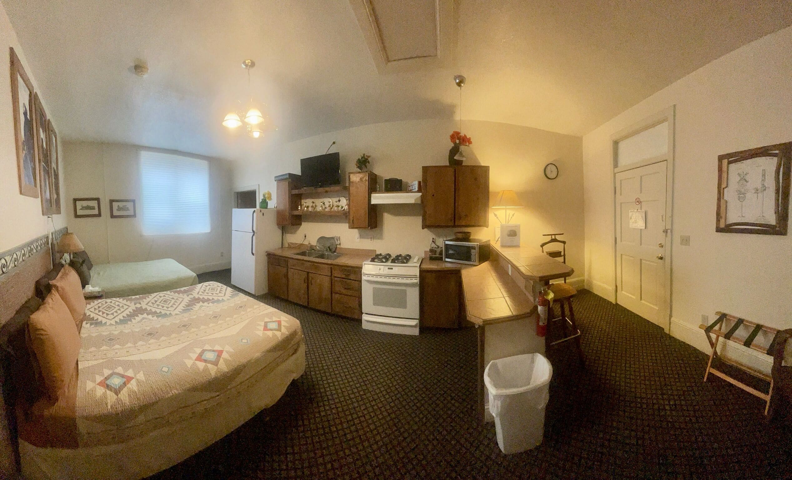 A compact room with a bed, kitchenette, and a small bathroom.