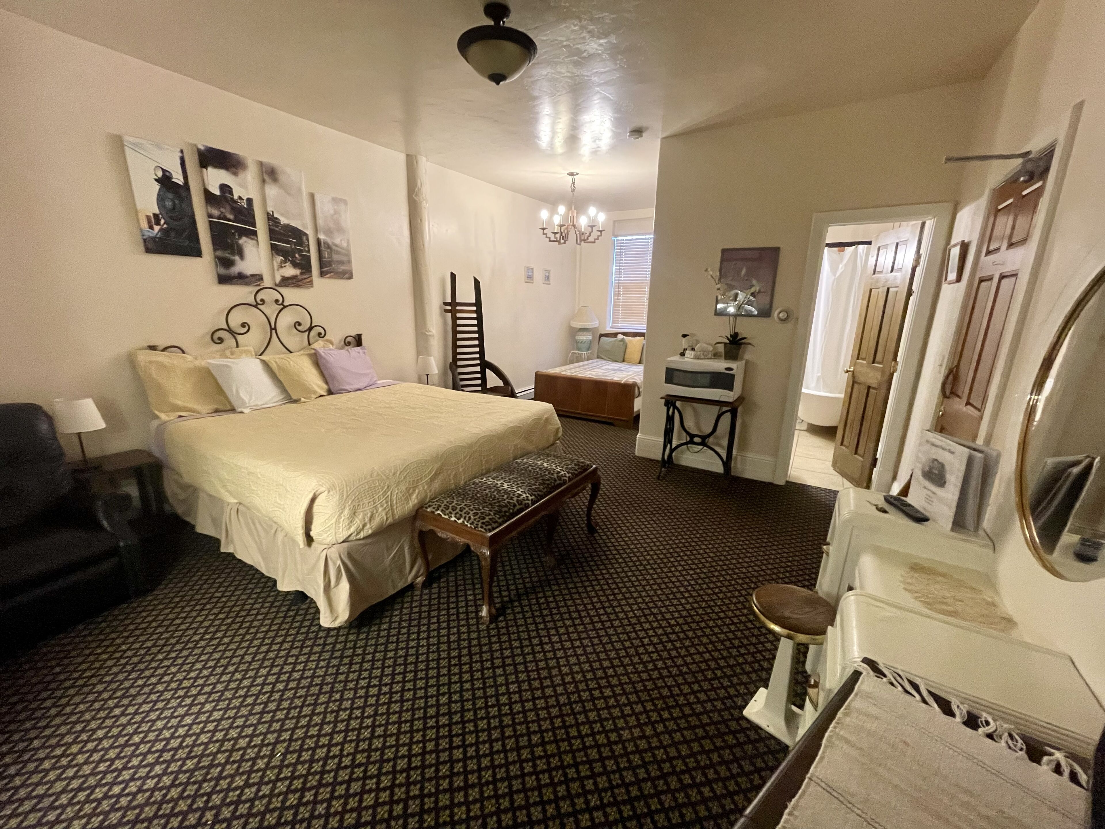 A bedroom with a bed, a bench, a desk, a chair, a mirror, and a dresser.