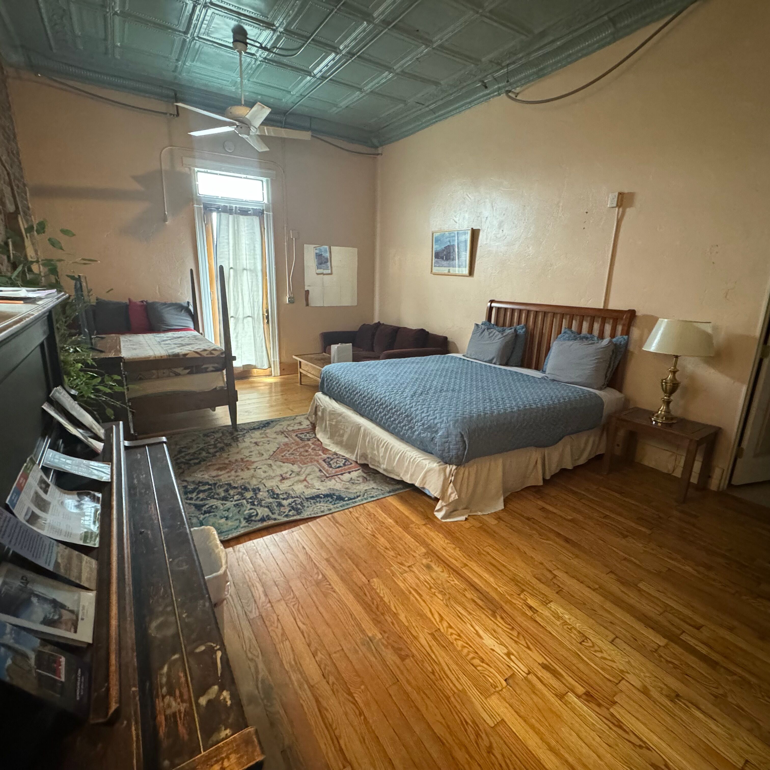 Une chambre à coucher comprenant un lit, un bureau, une chaise, un ventilateur de plafond, une fenêtre et une porte.