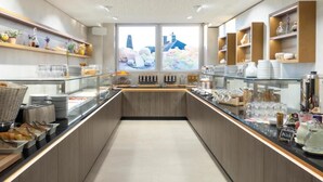 Una barra de desayuno moderna con vitrinas de vidrio, diversos alimentos y vistas panorámicas de la ciudad a través de amplias ventanas.