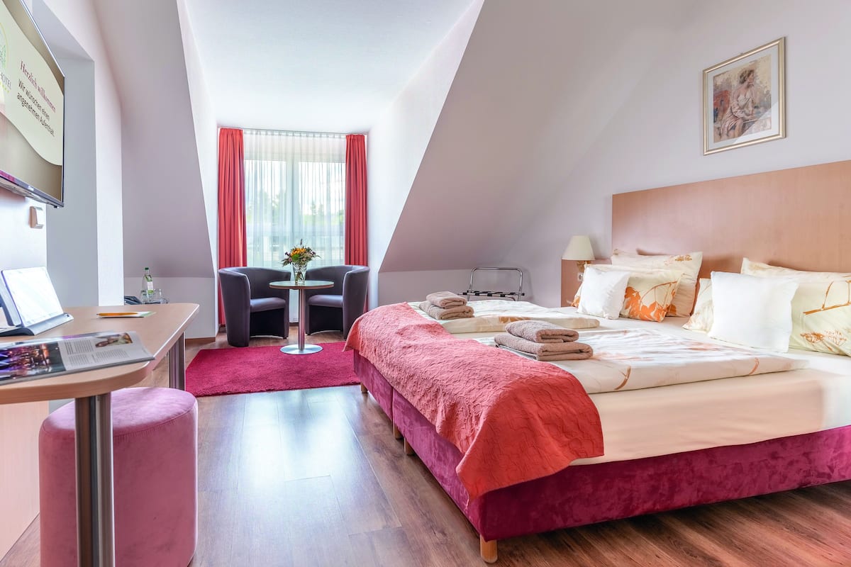 Una habitación de hotel moderna con una cama grande, un escritorio con una computadora portátil, una silla y una pequeña mesa con un florero.