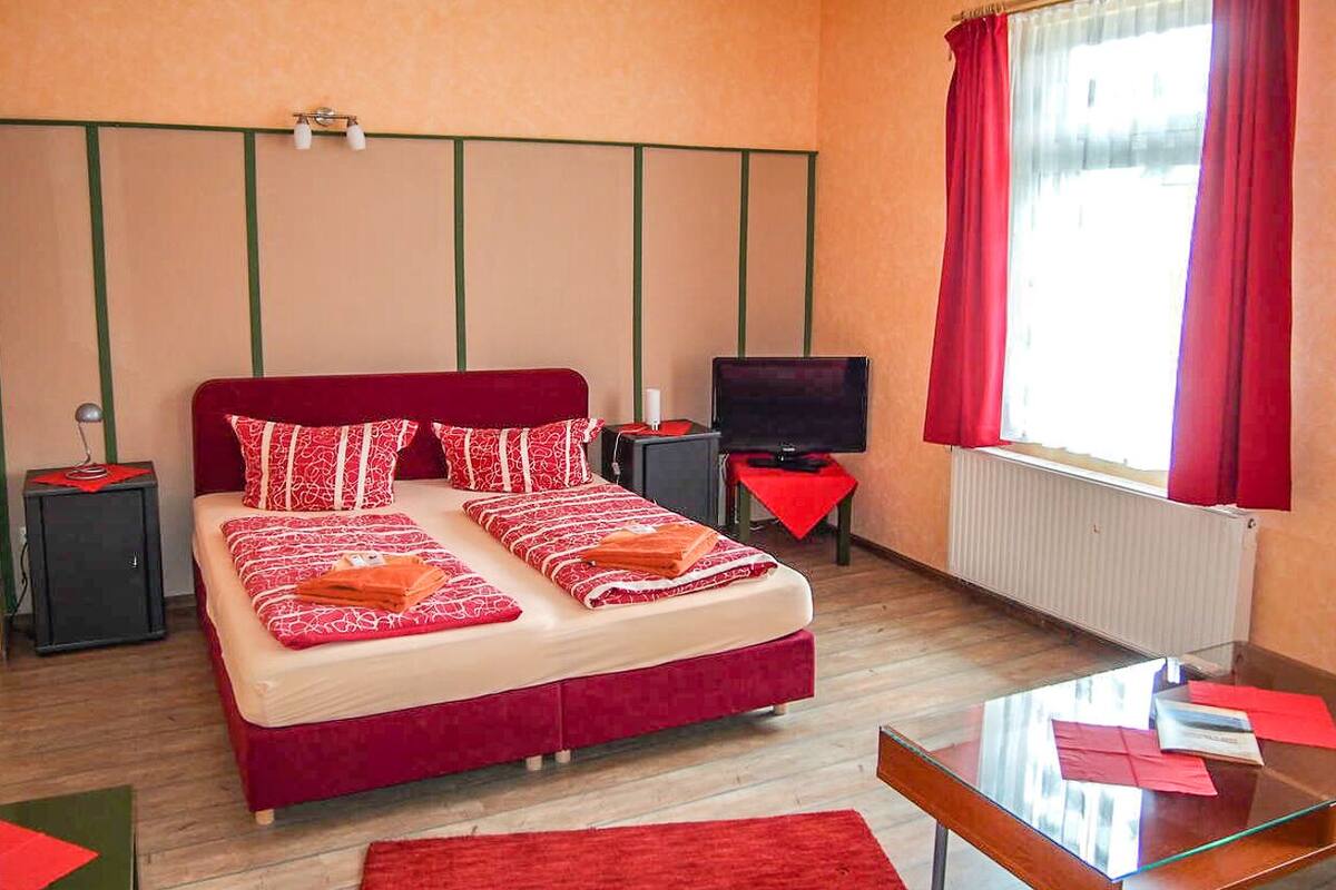 A hotel room with a large bed, a television, a desk, and a window with curtains.